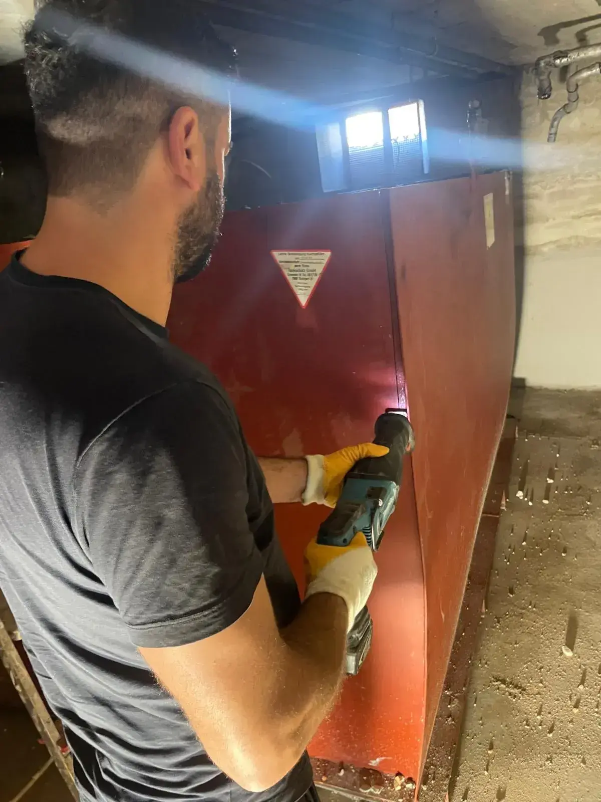 Handwerker zerlegt einen Öltank im Keller mit der Säbelsäge
